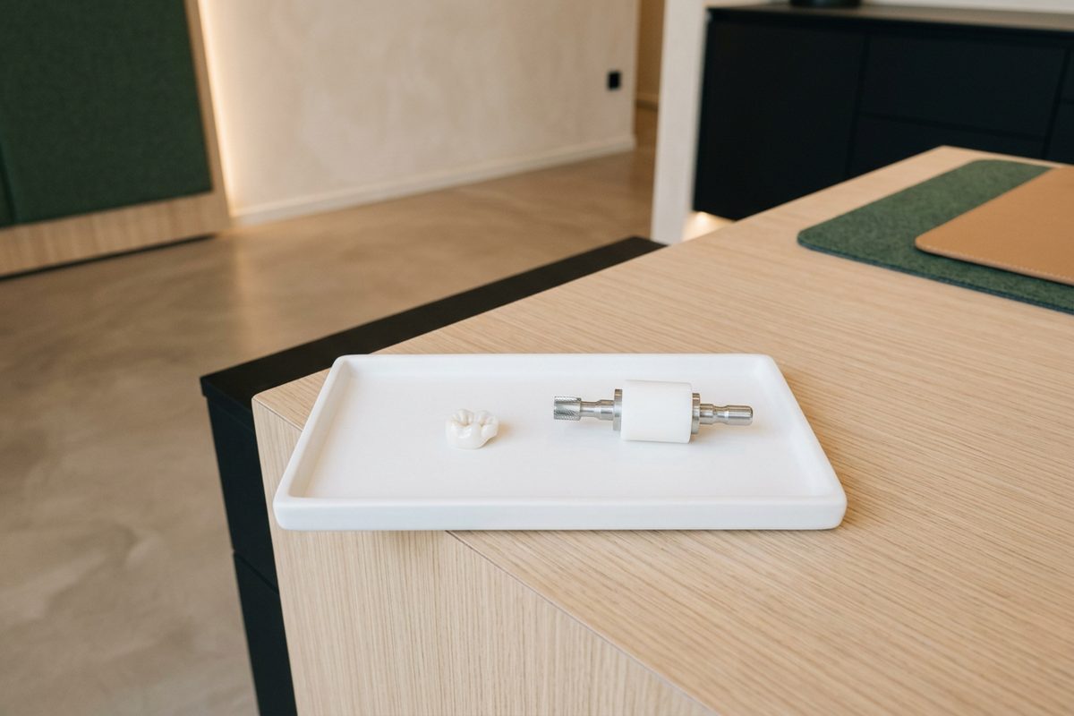 Illustrative object photograph of a milled ceramic onlay beside an unmilled ceramic block on its mandrel, on a white tray