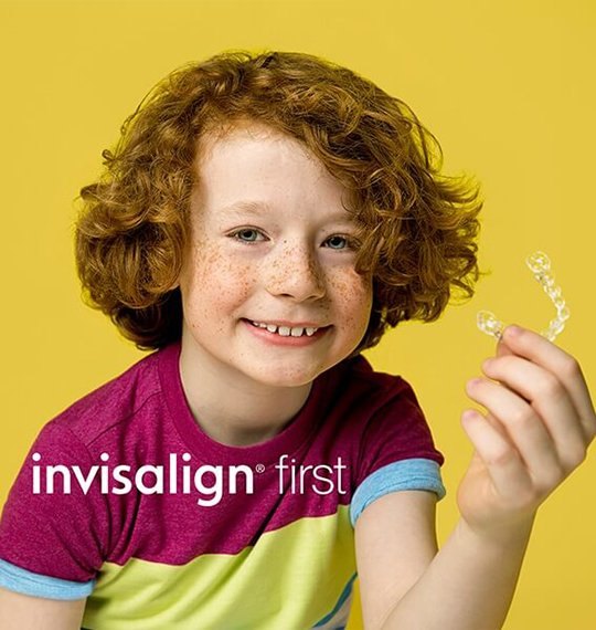 A child holding an Invisalign First clear aligner — manufacturer photograph, not taken at the clinic